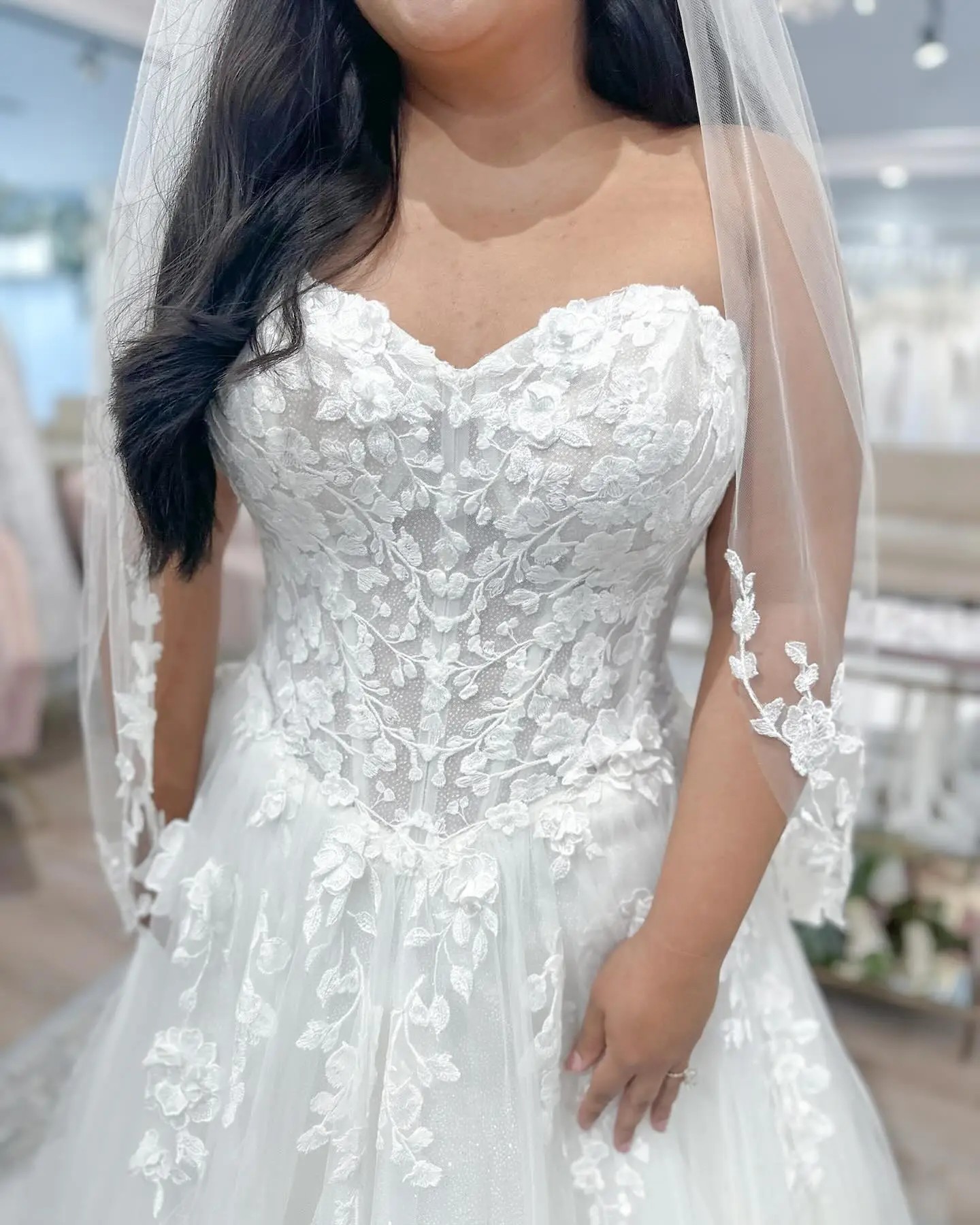 Model is wearing a strapless lace wedding dress with a basque waist. 