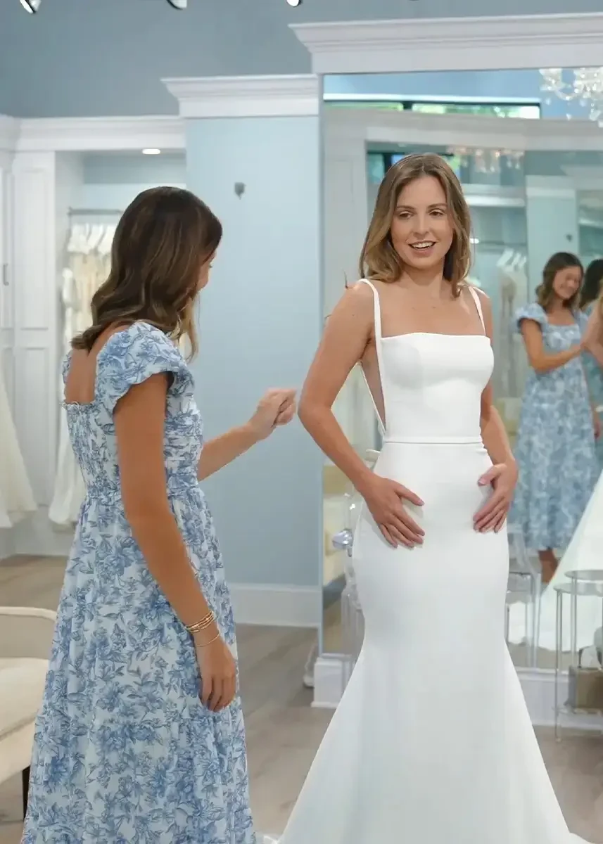 image shows a bride trying on a wedding dress with a stylist