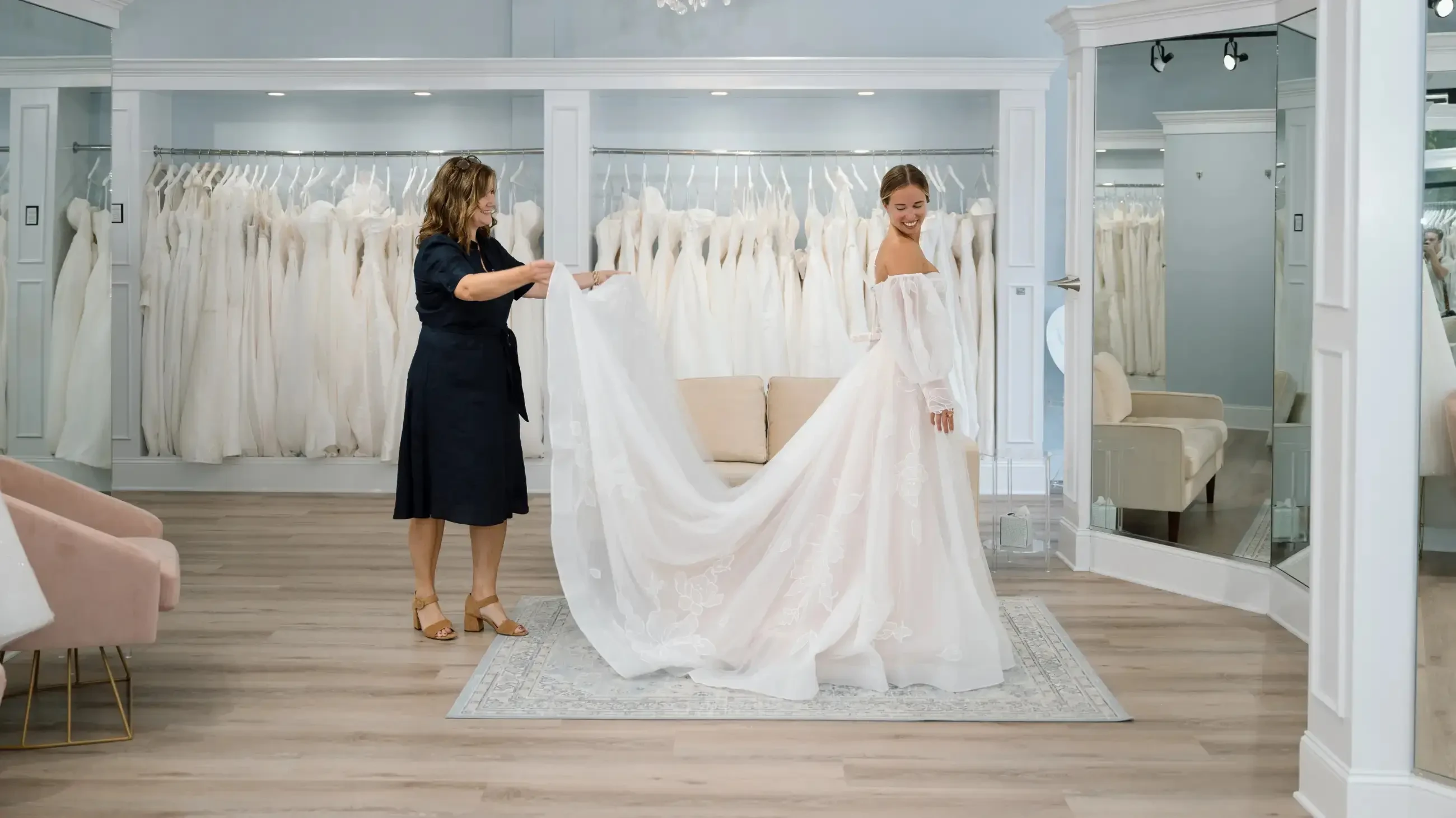 image shows a bridal stylist helping a bride try on a wedding dress