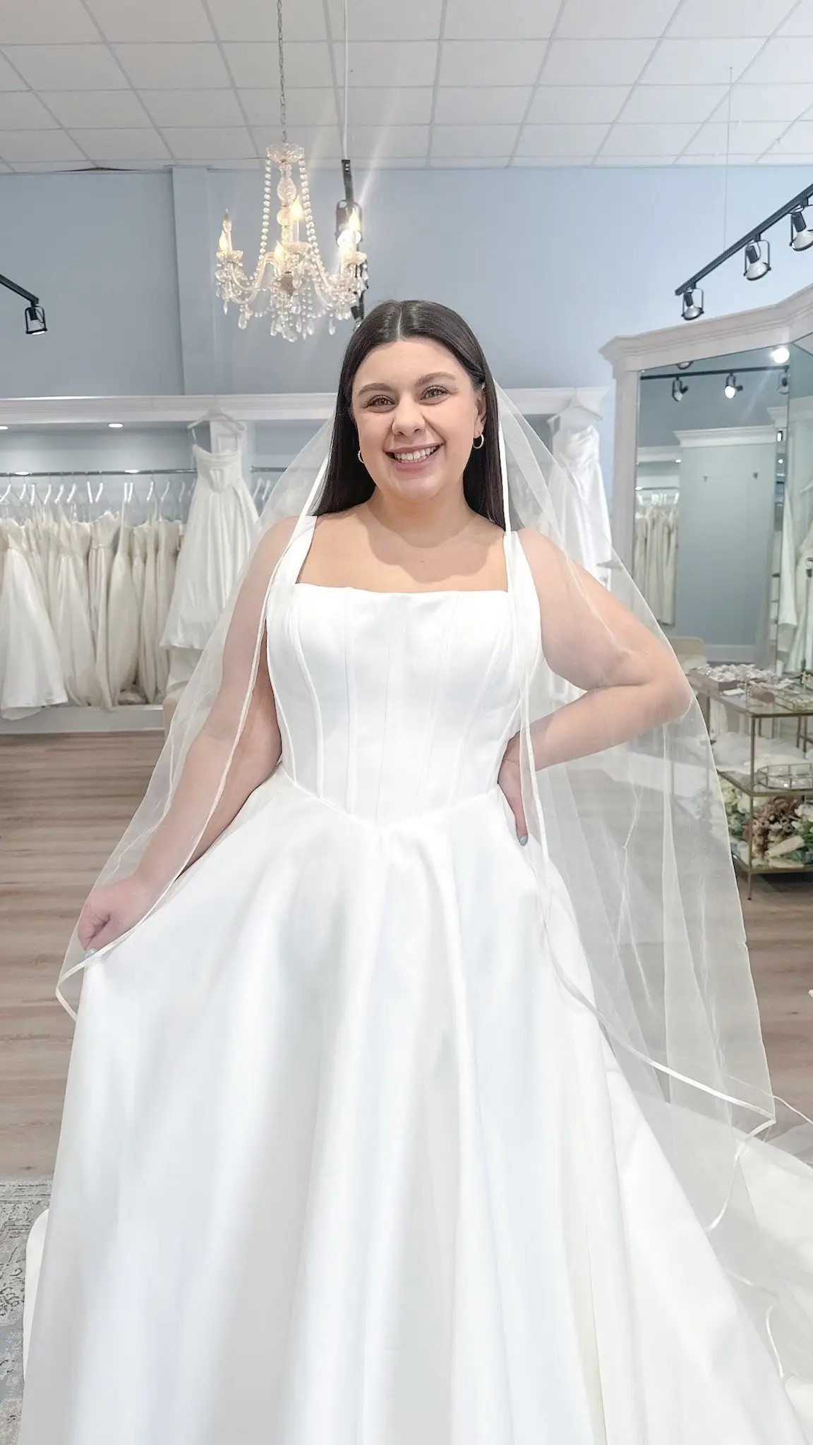 Model is wearing a sleeveless wedding dress with an a-line silhouette, square neckline, and dropped waist